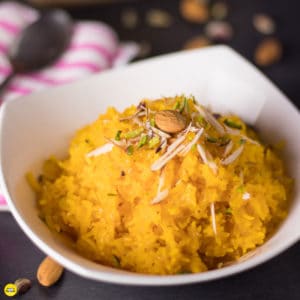 sweet kesaria rice in a white bowl on a black surface with chopped almonds and pista spread over to garnish