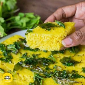Instant Khaman Dhokla on a dark surface with tempering of mustard seed, curry leaves and chilli |