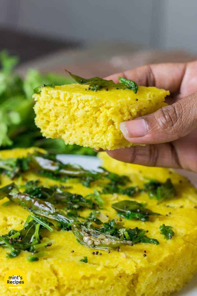 Instant Khaman Dhokla on a dark surface with tempering of mustard seed, curry leaves and chilli |