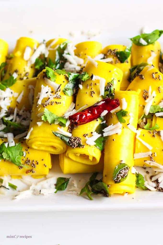 Khandvi on a white plate, garnished with some tempering of mustard seed and grated coconuts
