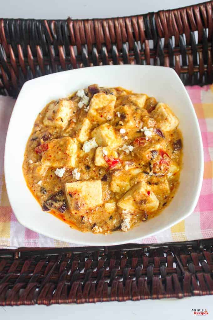 Khoya paneer in a deep vessel with some paneer crumbs on top for garnishing on a wooden surface with an handkerchief with a spoon l