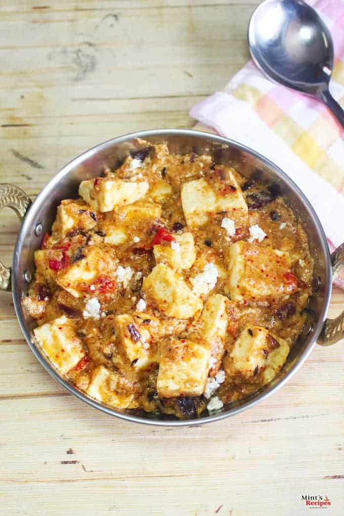 Khoya paneer in a deep vessel with some paneer crumbs on top for garnishing on a wooden surface with an handkerchief with a spoon l