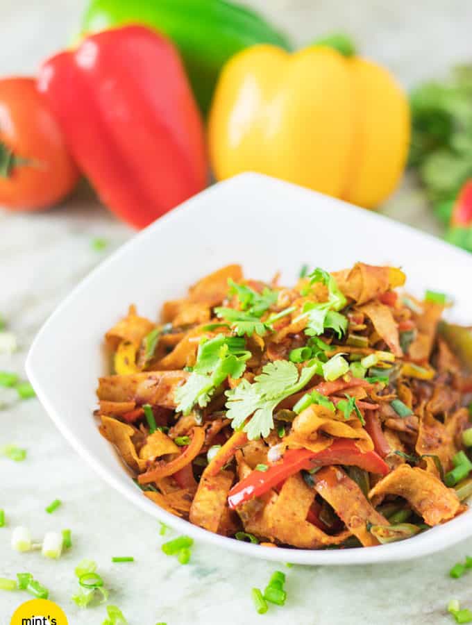 Roti noodles on a white bowl full with roti noodles and garnished with coriander leaves with a light background