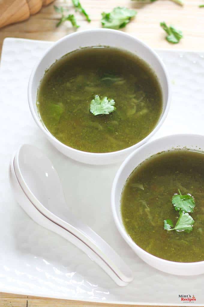 Lemon Coriander Soup on a white bowl kept on a black tray with a spoon and lemon slice and garnished with coriander leaves |