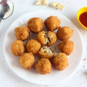Macaroni cheese balls on a white plate with some black pepper sprinkles on it kept on a white surface |