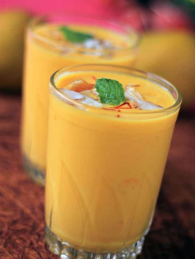 Mango Lassi on a glass with some ice cubes and some saffron with a mint leaf on it|