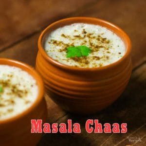 Masala Chaas in a clay pot with some cumin powder and coriander leaves and another masala chaas in the background kept on a wooden surface with some coriander leaves and chopped carrots to decorate the surface |