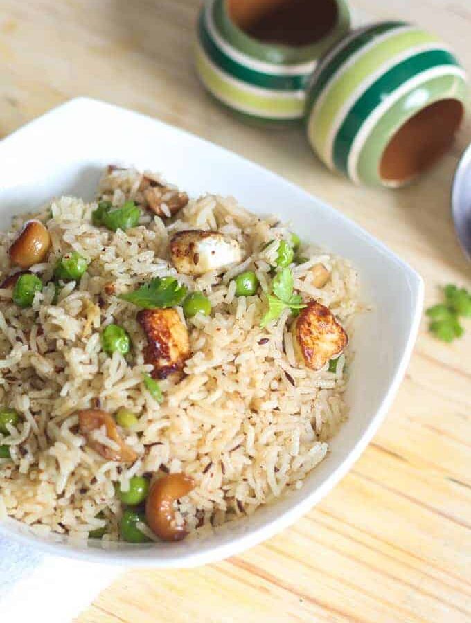 Matar paneer pulao in a white bowl with some coriander leaves kept on a wooden surface with top wooden bowls in the background |