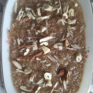 Meetha daliya on a white plate with lots of chopped cashew and almonds in it