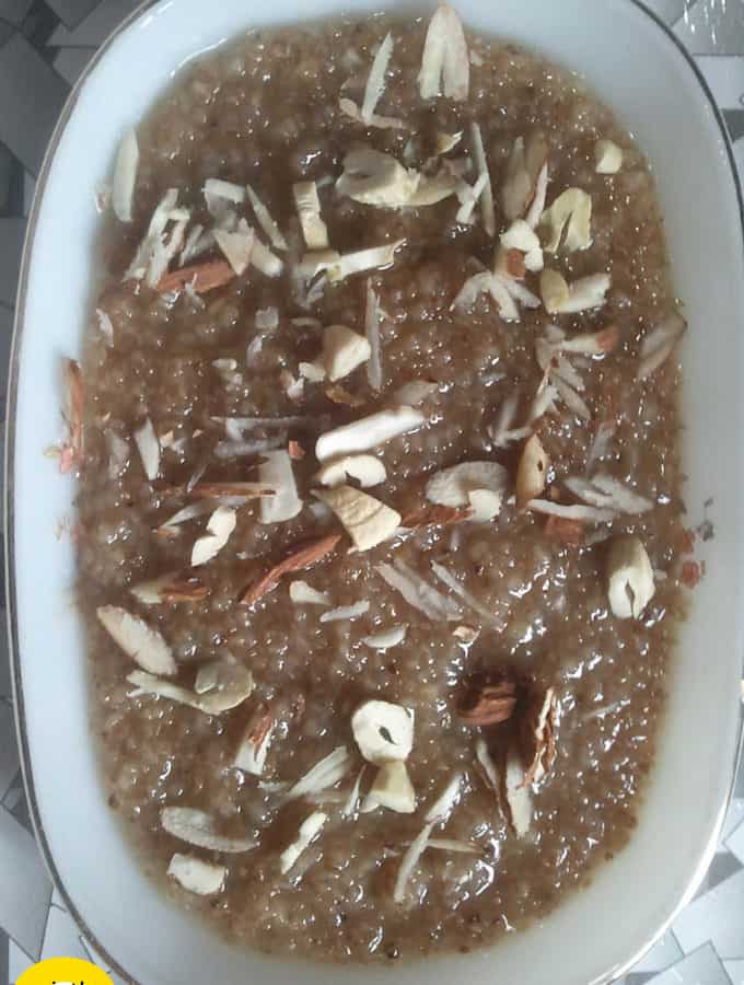 Meetha daliya on a white plate with lots of chopped cashew and almonds in it