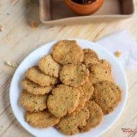 Methi Mathri on a white plate with some mathri stacked one another with some mathri on the sides of it and some background props