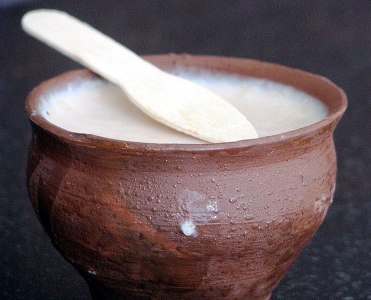 Mishti doi on a clay pot with a wooden spoon in a dark background |