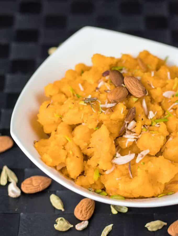 Moongdal ka halwa on a yellow bowl garnished with some chopped almonds keeped on a red hankerchief with a dark background |