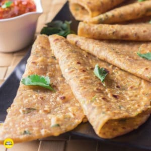 Sabut moongdal ka paratha on a black tray with some coriander leaves and some pickles on the background