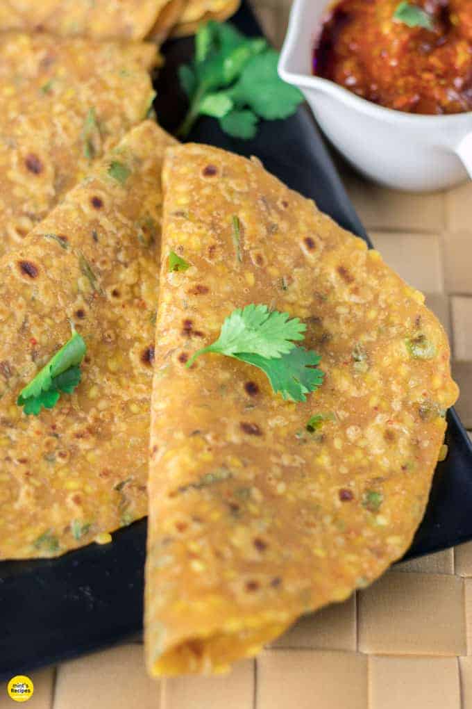 Sabut moongdal ka paratha on a black tray with some coriander leaves and some pickles on the background 