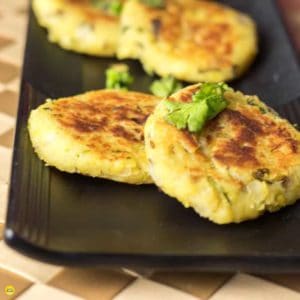 Moong dal ki tikki on a black tray with some moongdal tikki and garnished with some coriander leaves, kept on a brown colored mattress