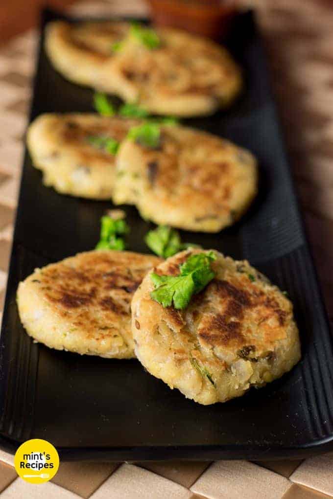 Moong dal ki tikki on a black tray with some moongdal tikki and garnished with some coriander leaves, kept on a brown colored mattress 