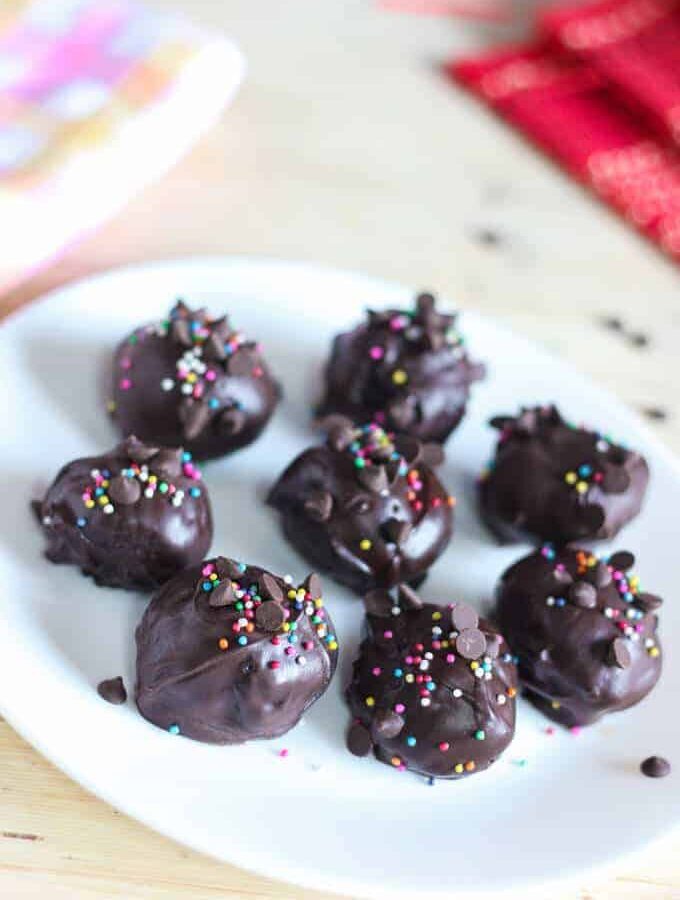 Oreo biscuits balls on a white plate with some chocolate biscuits ball and some sprinklers with choco chips kept on a wooden surface