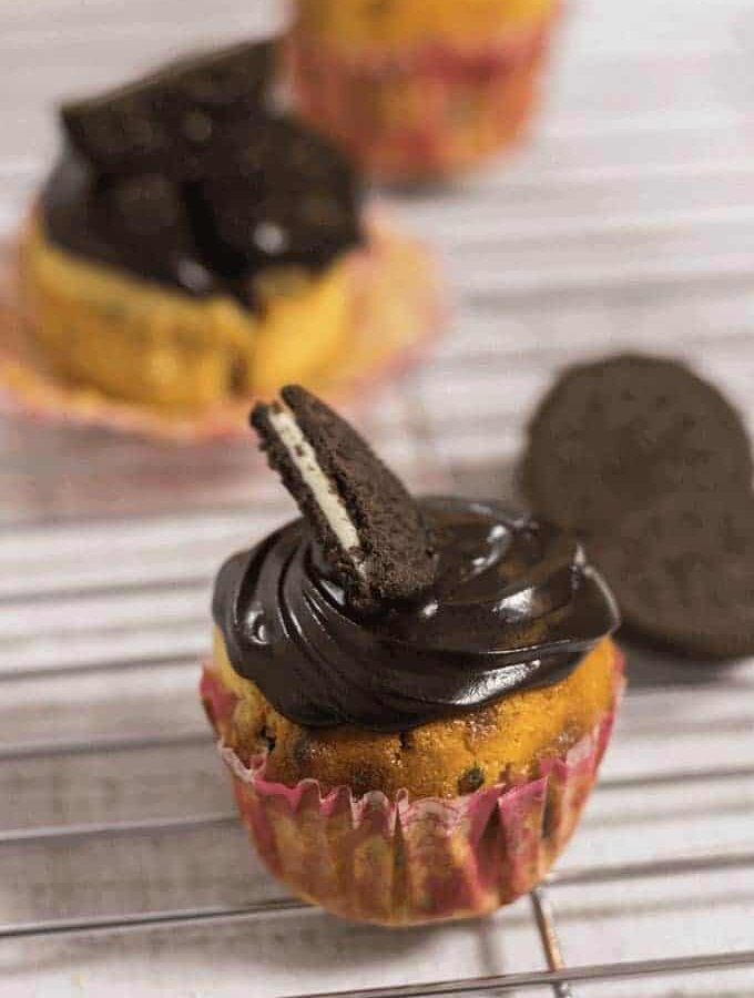 Oreo Cupcake on a steel rods with frosting of chocolate ganache and half oreo biscuits on it and some oreo cupcakes on the background |