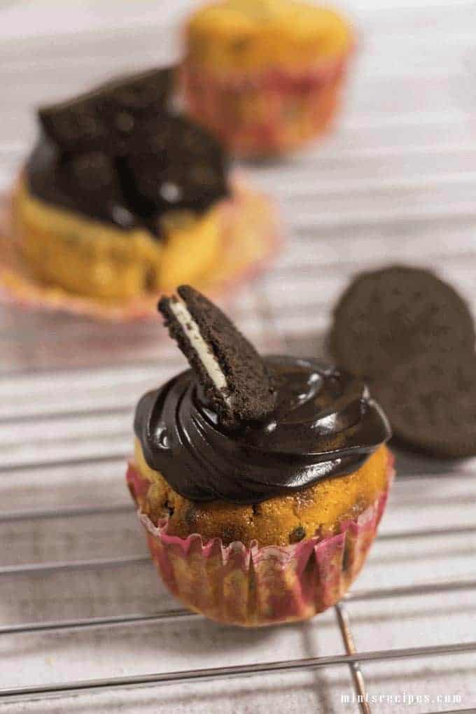 Oreo Cupcake on a steel rods with frosting of chocolate ganache and half oreo biscuits on it and some oreo cupcakes on the background |
