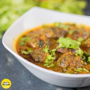 Palak paneer kofta curry on a white bowl with some sprinkles of coriander leaves and some coriander leaves and tomatoes kept on a black wooden surface |
