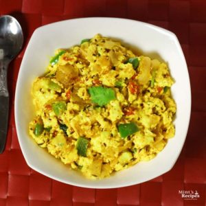 Paneer Bhurji on a white bowl kept on a red color mattress with some garnishing of coriander leaves |