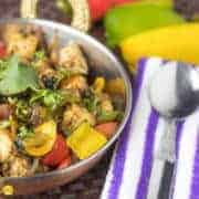 paneer capsicum masala on a deep vessel garnished with some coriander leaves on a dark mat with some yellow and red bell peppers and green capsicum with a spoon on a handkerchief |