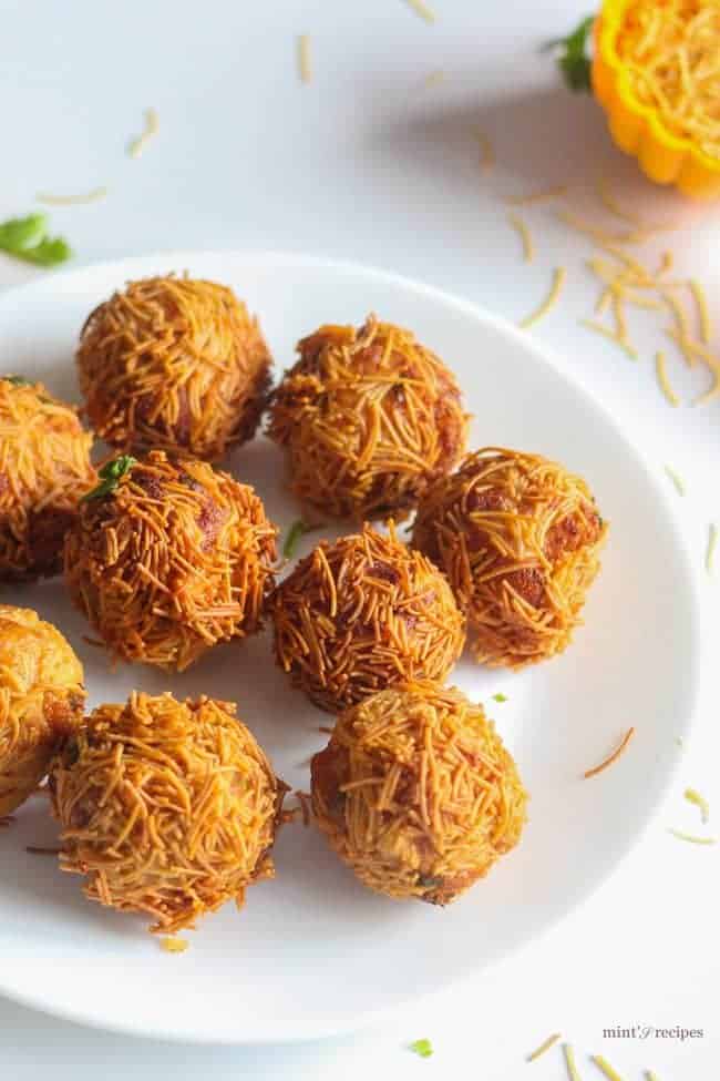 Paneer Vermicelli Balls on a white plate with some sev sprinklers garnished with some coriander leaves 