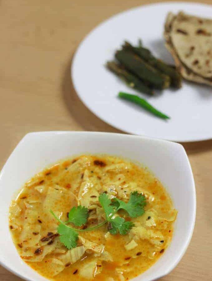 Papad Ki Sabzi on a white bowl with some coriander leaves on it and in the background a white plate with some roti and ladyfinger's fry on it