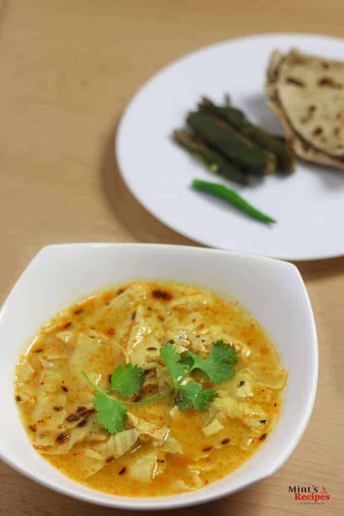 Papad Ki Sabzi on a white bowl with some coriander leaves on it and in the background a white plate with some roti and ladyfinger's fry on it 