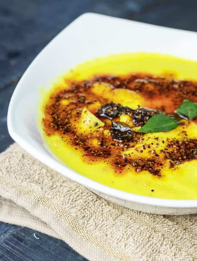 Papad mangodi curry on a white plate with little tempering of mustard seed, curry leaves, and red chilli powder, garnished with few curry leaves kept on a handkerchief on a wooden black surface|