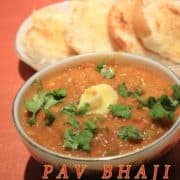 Indian Pav Bhaaji on a white surface wit for pav pieces on a white tray and a bowl full of bhaji with little butter and garnished with some coriander leaves and a spoon,fork in both side oh pav bhaji |