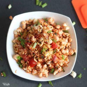 Popcorn Bhel on a white bowl with lots of veggies and sev for garnish.|