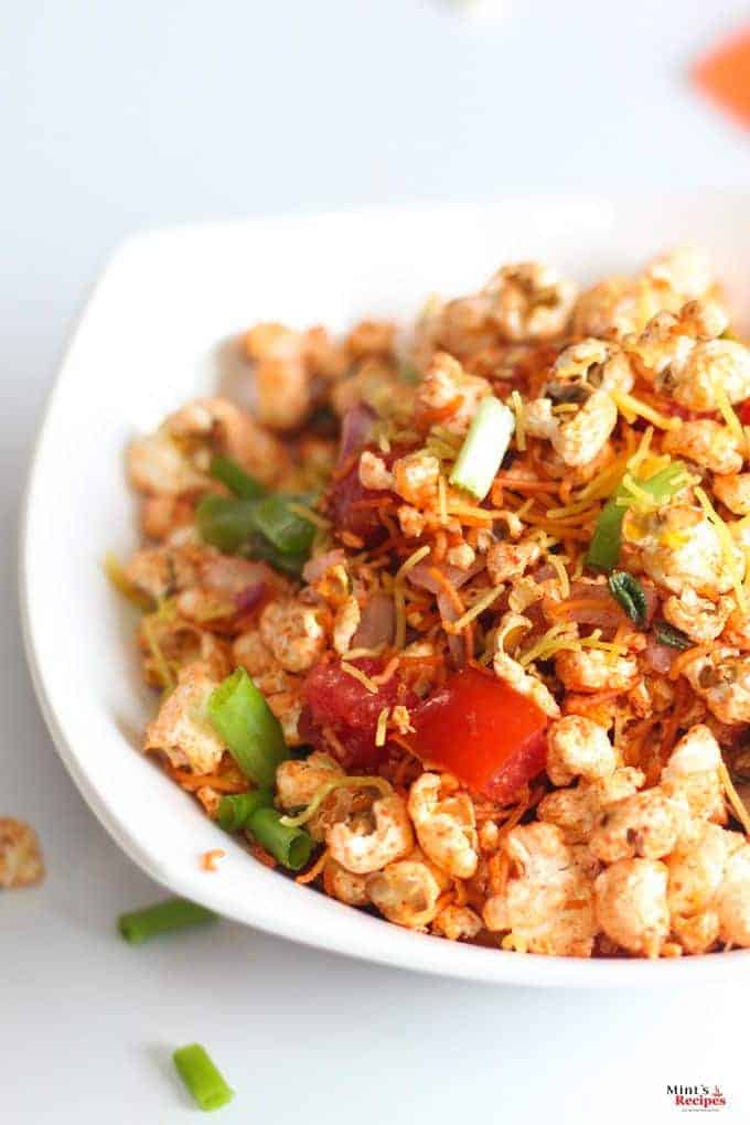 Popcorn Bhel on a white bowl with lots of veggies and sev for garnish.|