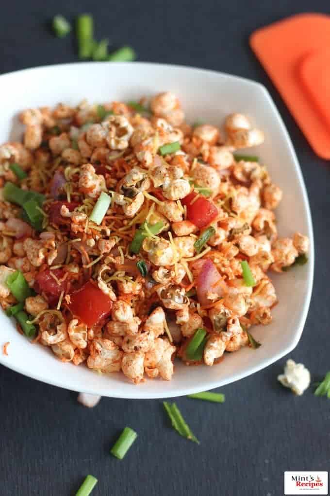 Popcorn Bhel on a white bowl with lots of veggies and sev for garnish.|