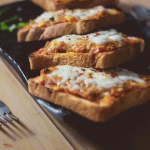 Potato Cheese Toast on a black tray with some garnishing of chili flakes kept on a wooden surface with a dark background