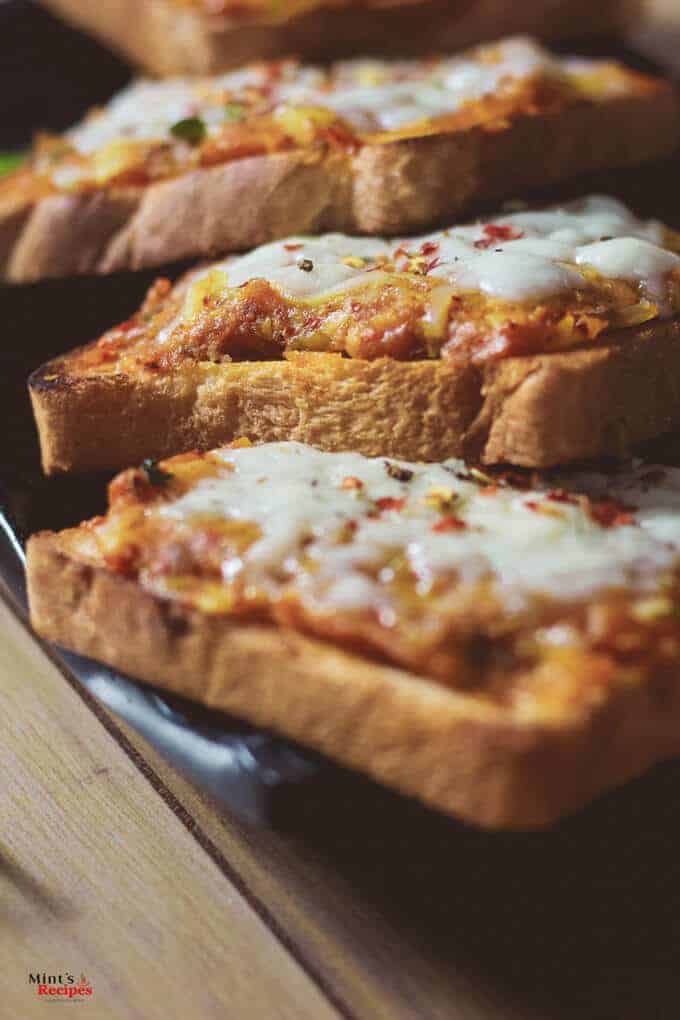 Potato Cheese Toast on a black tray with some garnishing of chili flakes kept on a wooden surface with a dark background 