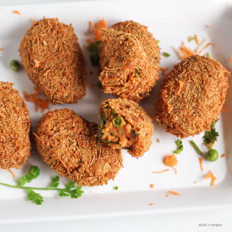 Potato Vermicelli Cutlet on a white rectangular plate with some grated carrots and some coriander leaves