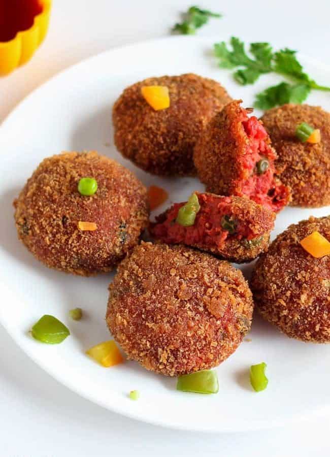 Red Velvet Cutlet on a white plate with some veggies and some coriander leaves with some tomato ketchup in a plastic bowl