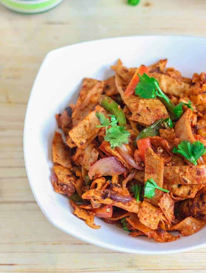 Roti noodles on a white bowl full with roti noodles and garnished with coriander leaves with a light background