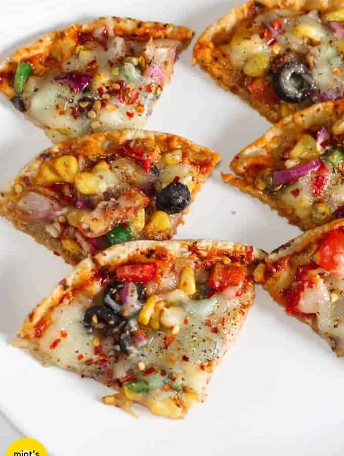 Roti pizza on a white plate with slices of roti pizza places one by one in a queue, garnished with some black pepper, red chili flakes, and some oregano |