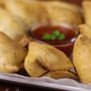 Samosa on a white tray with some tissue paper and little tomato ketchup on the center of the plate with rounded into samosas kept on a dark wooden surface |