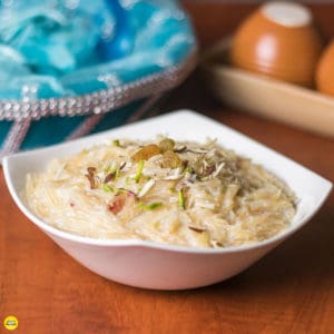 Sewai Kheer Recipe| Sewai served on a white bowl garnished With Almonds,Pistachious and raision Over A red mat lined With Black And Creamy Coloured Strings.