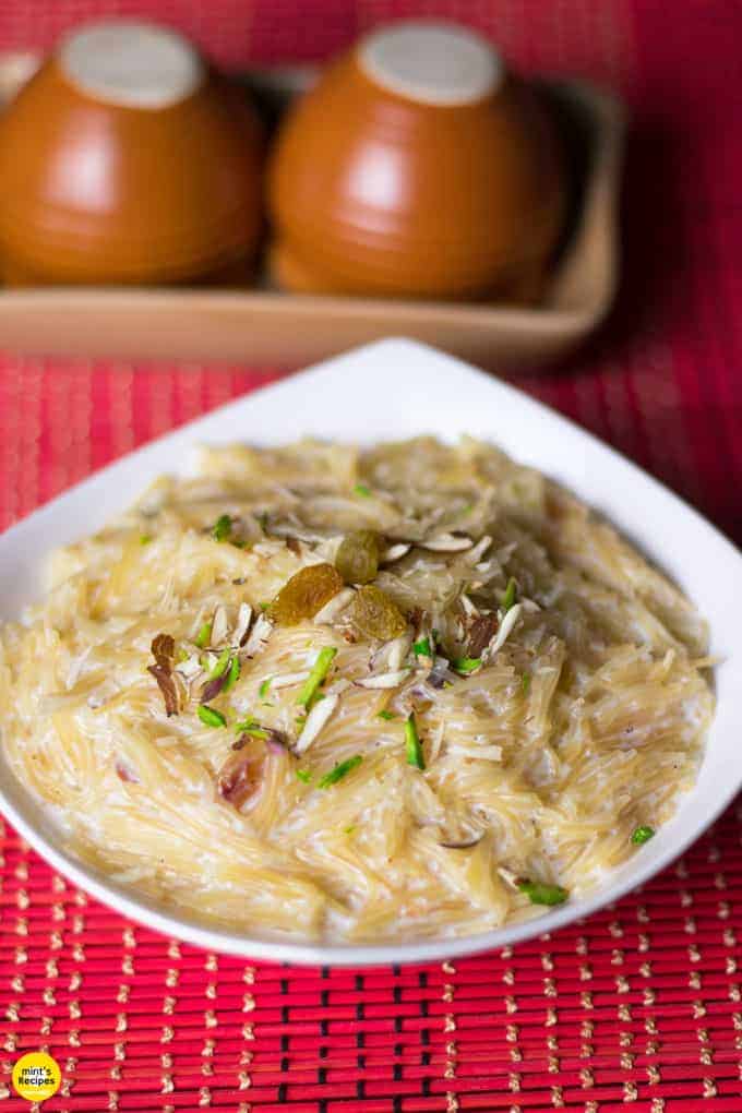 Sewai Kheer Recipe| Sewai served on a white bowl garnished With Almonds,Pistachious and raision Over A red mat lined With Black And Creamy Coloured Strings.