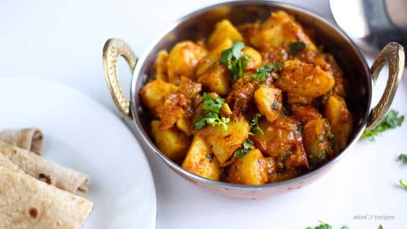 Spicy Potato Curry on a deep vessels garnished with some coriander leaves on a white surface and spread some coriander leaves |