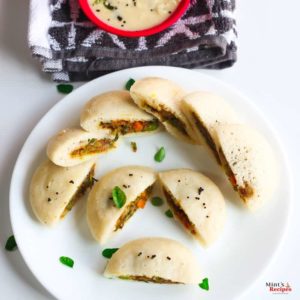 Stufffed Rava Idli on a white plate with some curry leaves and some coconut chutney