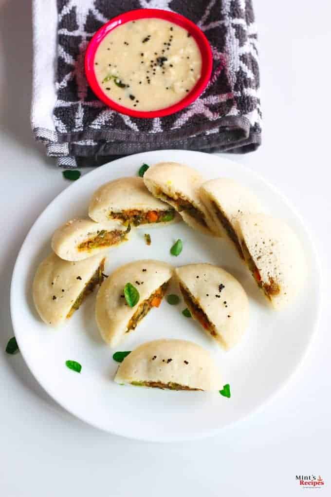 Stufffed Rava Idli on a white plate with some curry leaves and some coconut chutney