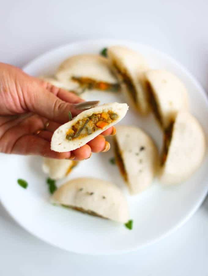 Stufffed Rava Idli on a white plate with some curry leaves and some coconut chutney