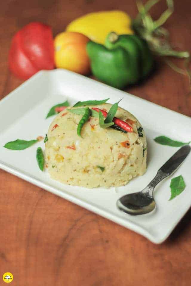 Suji upma on a white plate with dark background and some bell peppers