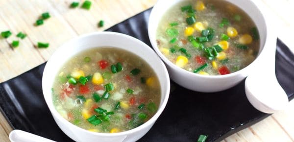 Sweet Corn Soup on a white bowl putted in a blake tray with soup spoon garnished with some spring onions | www.mintsrecipes.com |